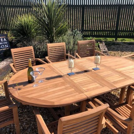 Teak extending oval garden dining table with eight matching slatted armchairs in a landscaped garden