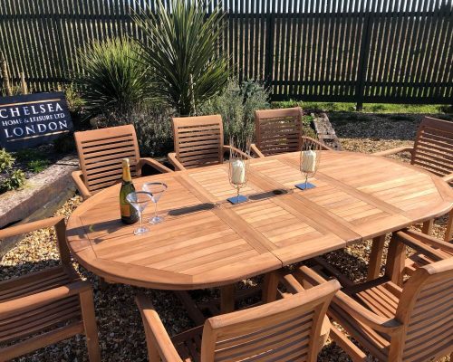 Teak extending oval garden dining table with eight matching slatted armchairs in a landscaped garden
