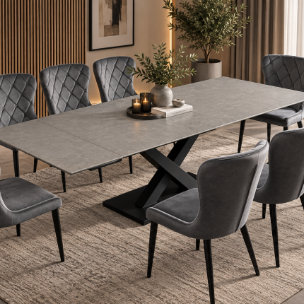 Large grey extending dining table with black X-frame pedestal base and eight grey button-back upholstered dining chairs